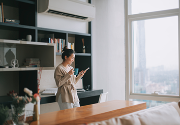 woman standing holding cup looking at phone.